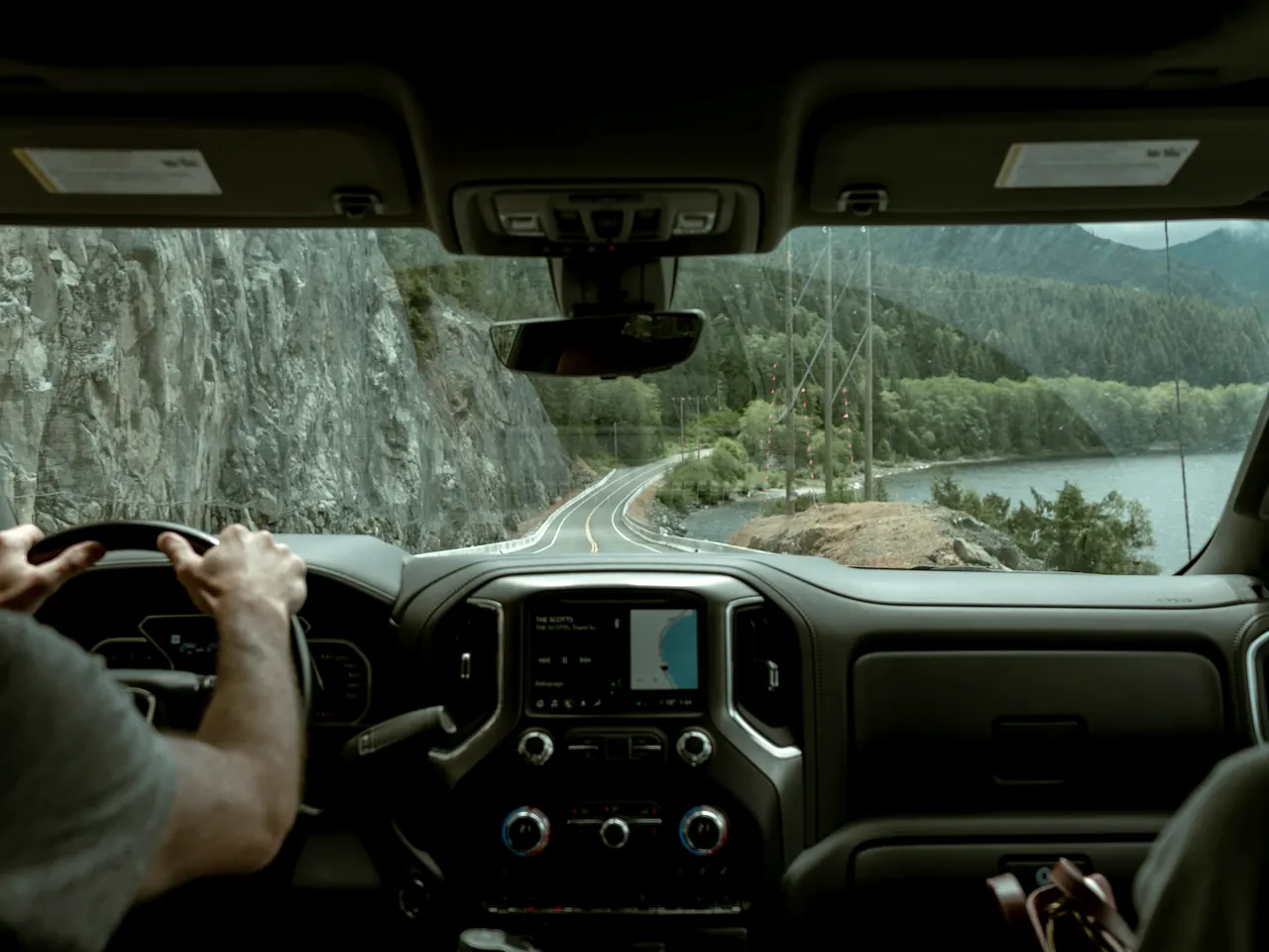 Interior de la cabina de un camión en ruta: las manos del conductor en el volante y el camino por delante a través del parabrisas, que son las dos vistas que toman la cámara DMS y la ADAS.